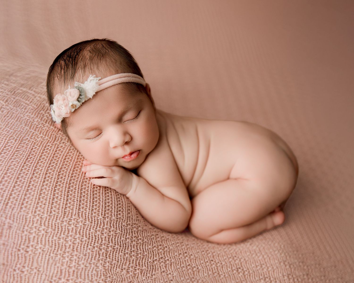 Sleeping newborn baby in soft pink tones photographed in multiple artistic poses on textured blanket.