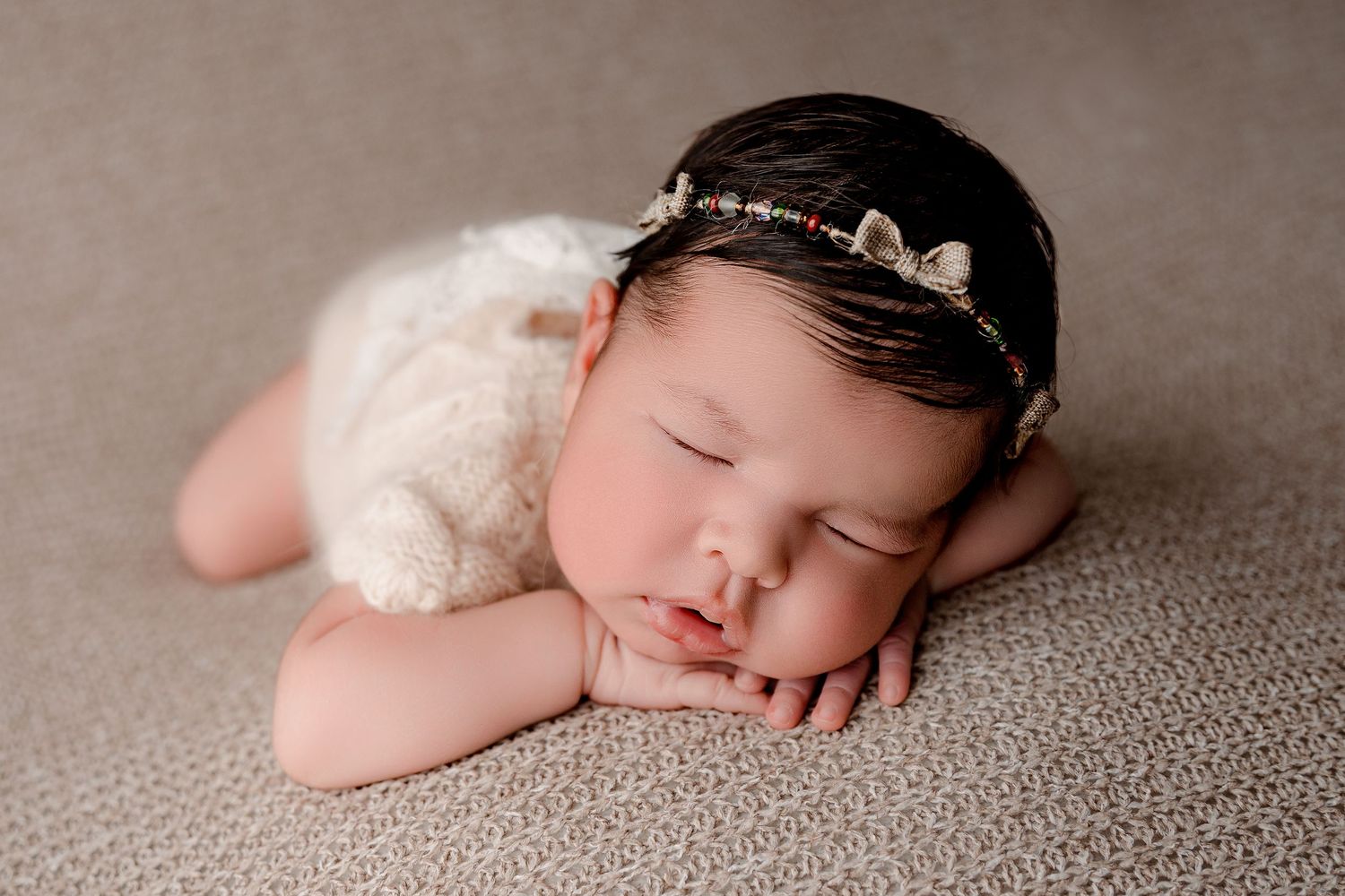 Sleeping baby wearing crown headpiece on textured brown backdrop.
