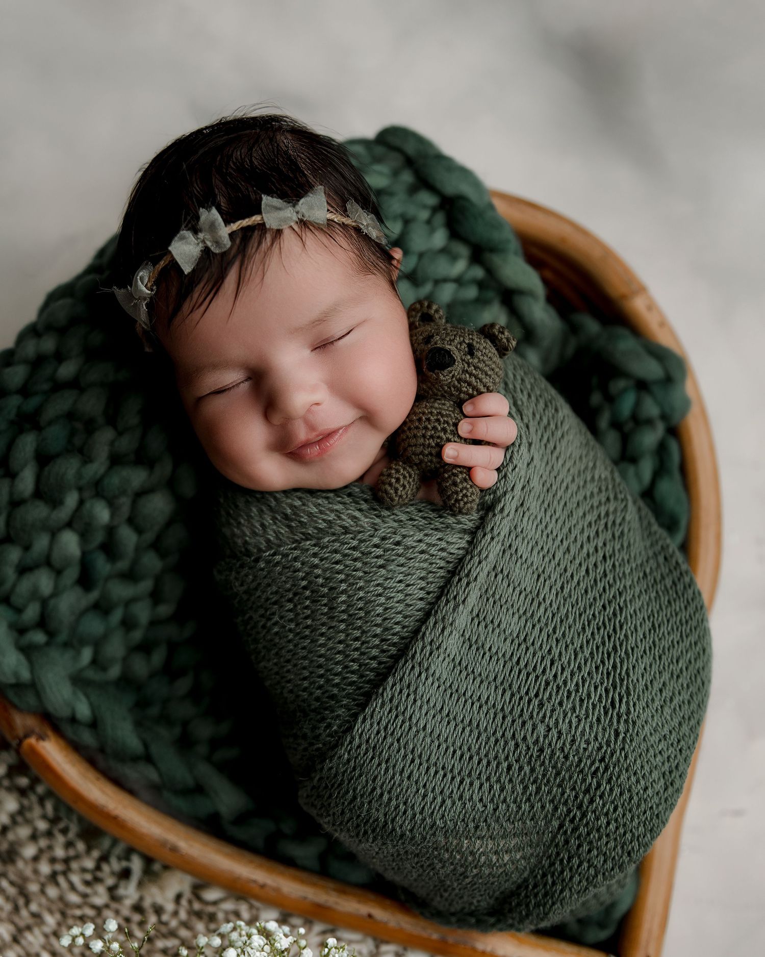 Peaceful newborn wrapped in green knit blanket sleeping in wooden basket with chunky knit accents.