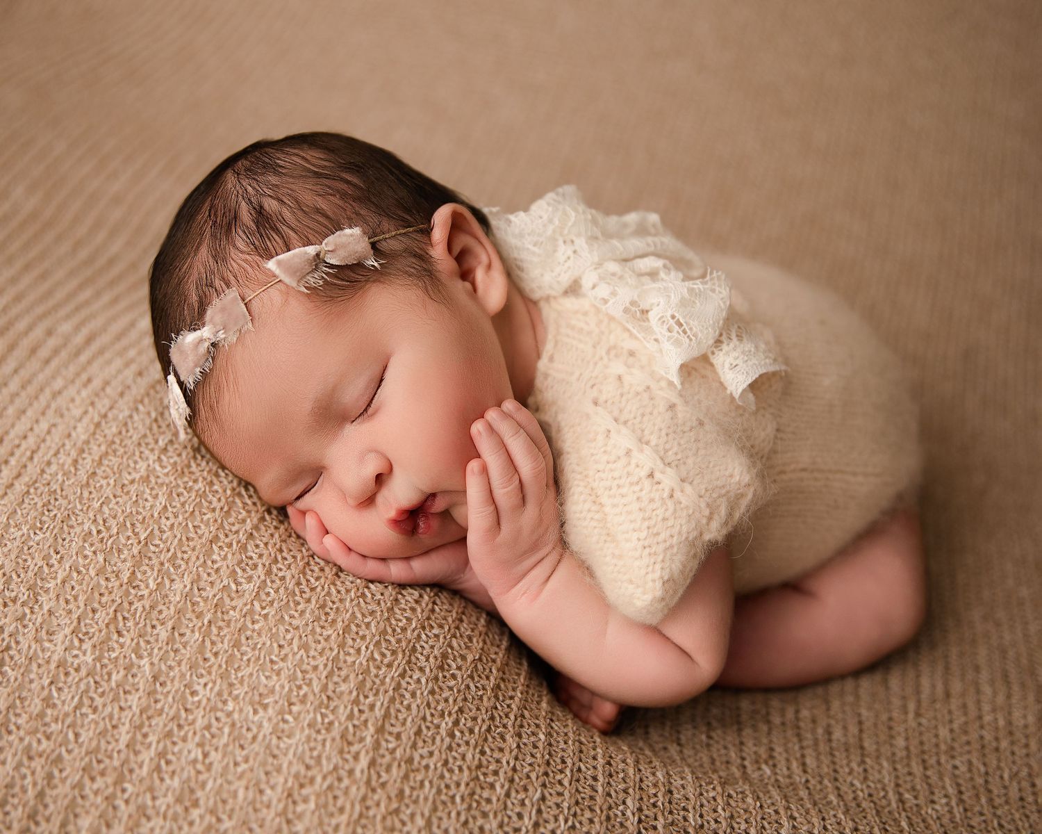 Peaceful sleeping newborn in cream lace outfit on brown textured surface.