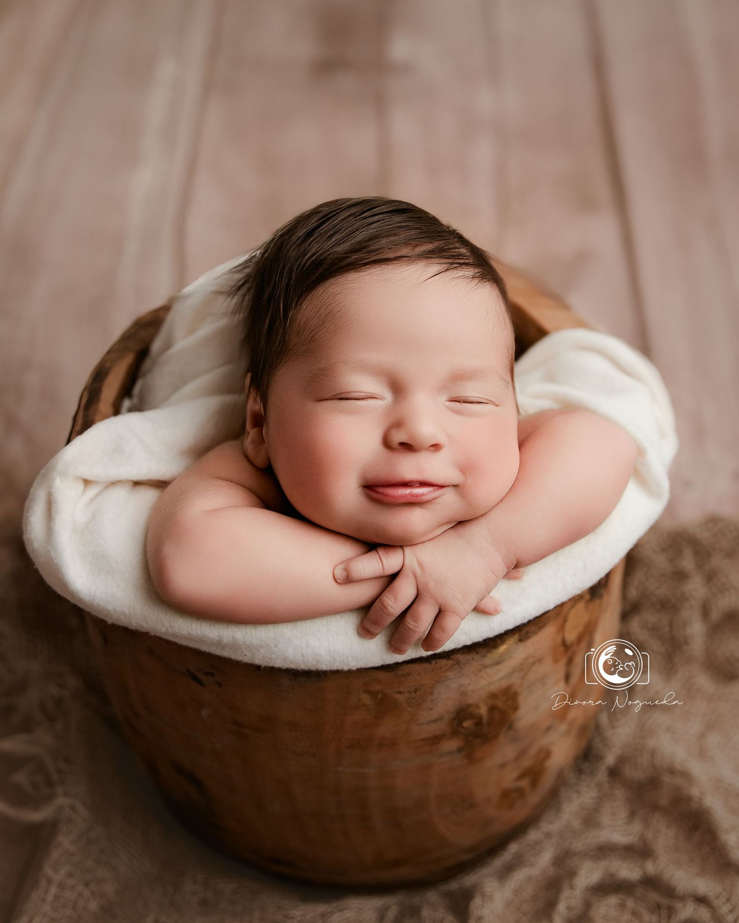 Sleeping newborn baby nestled in a rustic wooden bowl on textured brown backdrop during professional photoshoot.