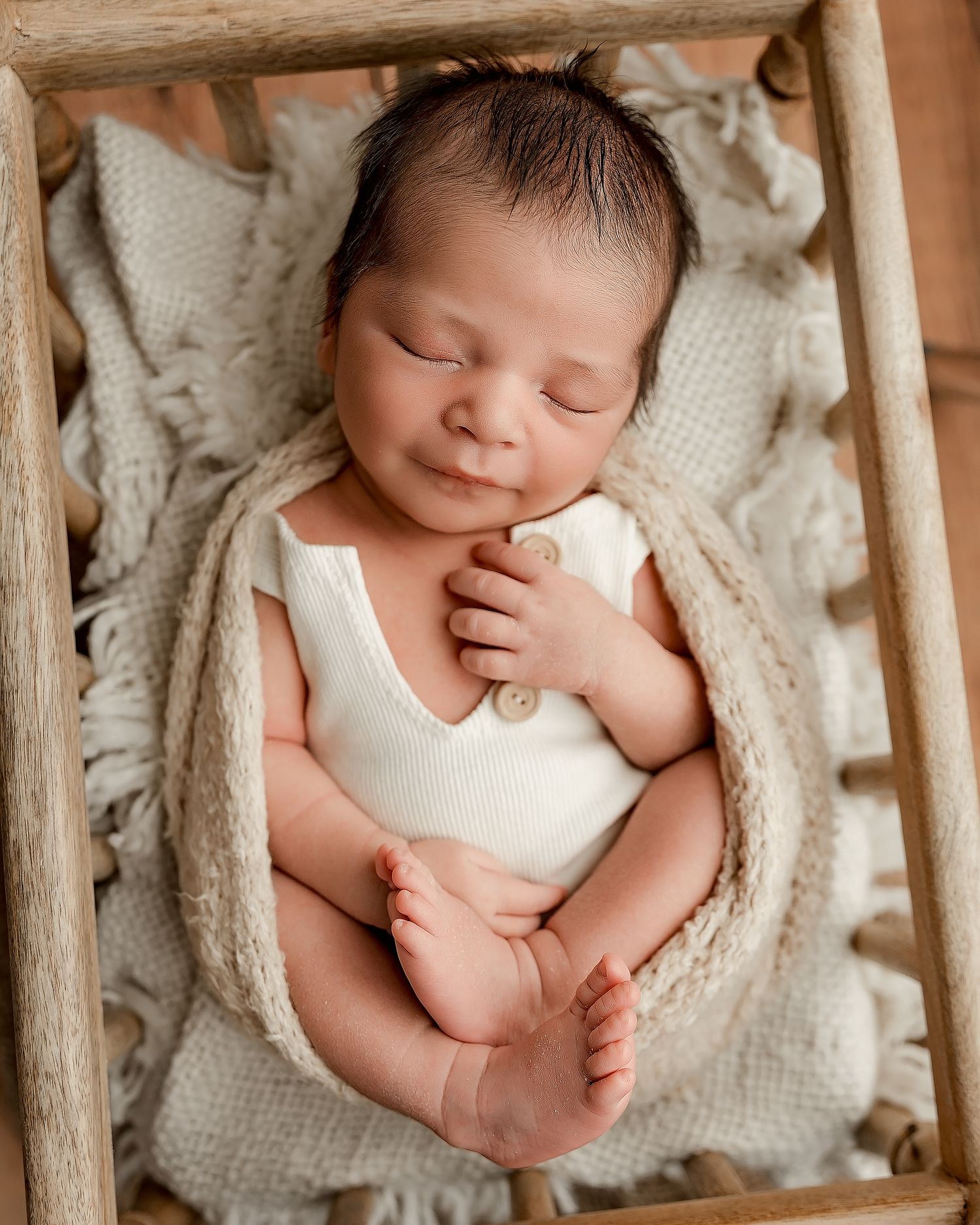 Sleeping newborn baby in cream romper nestled in wooden crate with knit blanket for professional newborn photography.