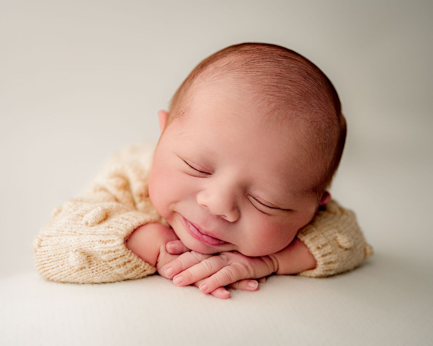 Sleeping newborn resting on cream knit sweater against light neutral background.
