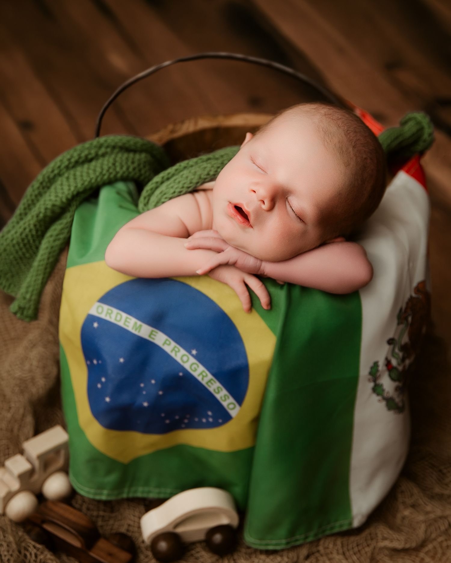 Sleeping newborn baby resting on Brazilian flag inside rustic bucket.