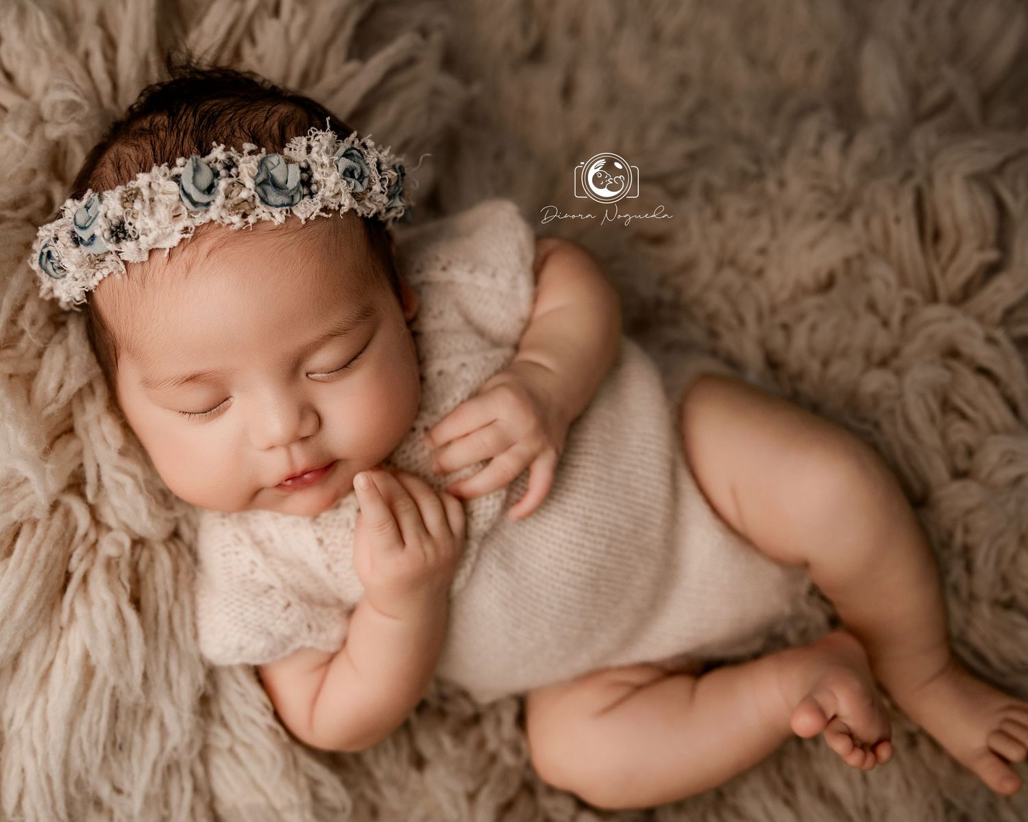 Sleeping newborn in beige outfit with crystal headpiece lying on soft fur backdrop in neutral tones.