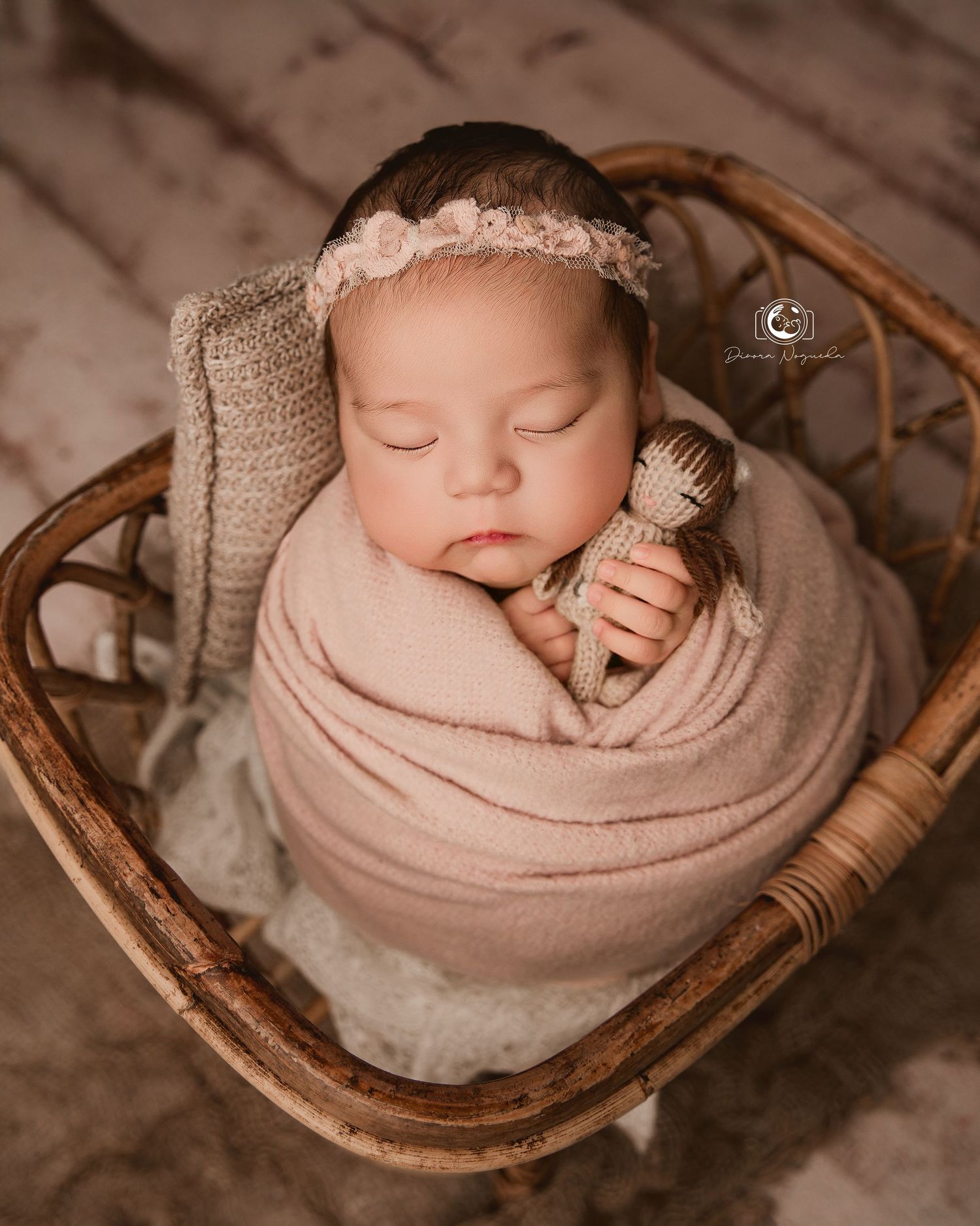 Peaceful newborn swaddled in beige wrap holding tiny brush, nestled in vintage wicker basket.