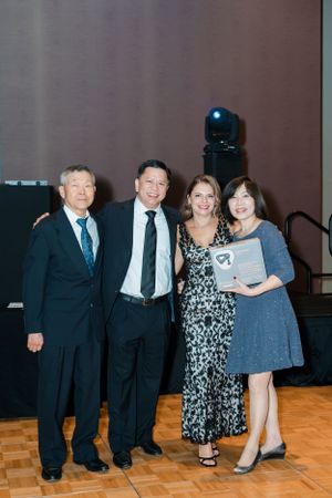 Four people posing together at a formal awards ceremony, with one person holding a framed recognition plaque.