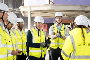 Construction workers in yellow hi-vis vests and white hard hats discussing plans on a building site.