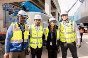 Four construction workers in yellow safety vests and hard hats pose together at an active construction site.