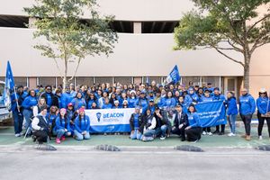 Large group of volunteers in blue Beacon shirts posing outdoors for a community service event photo.