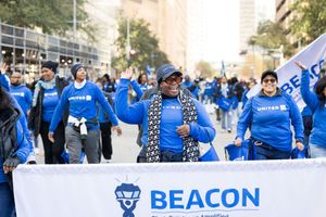 United Airlines BEACON group employees marching in blue uniforms at an outdoor parade event.