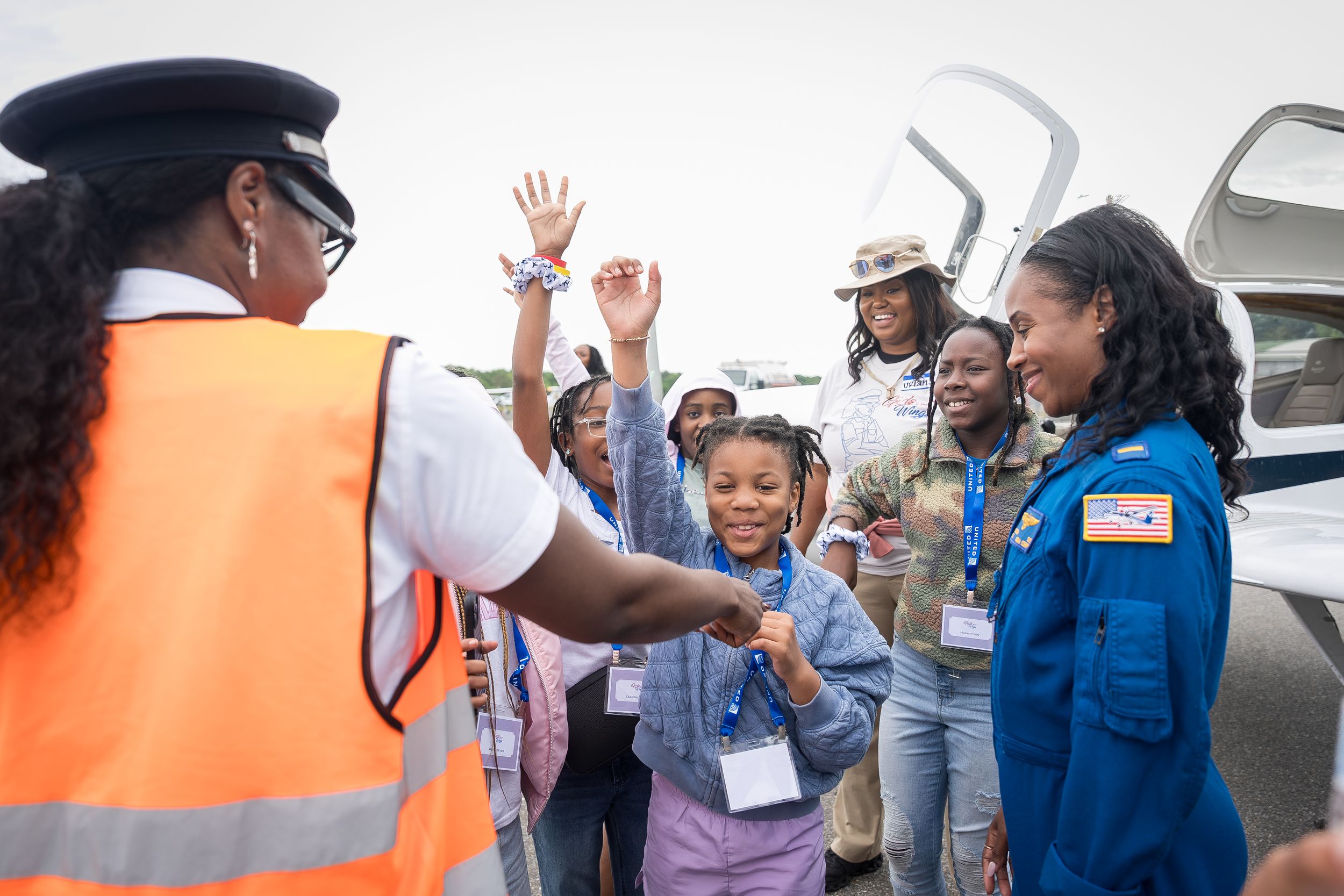 A female pilot and astronaut greet excited children near a small aircraft at an aviation event.