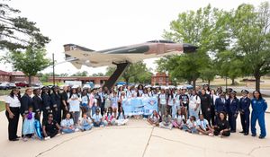 Large group of students and military personnel posing in front of a fighter jet display at an air force base.