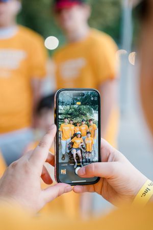Person photographing a group of youth volunteers in yellow t-shirts on a smartphone.
