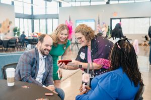 Group of professionals laughing and sharing content on a smartphone at an indoor networking event.