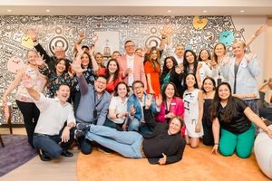 Large group of diverse professionals celebrating together in front of a vibrant artistic mural.