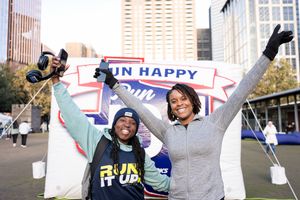 Two women celebrate at a Run Happy Ford running event, posing joyfully in front of a branded banner outdoors.