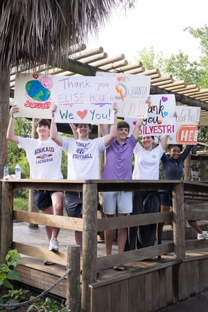 Students holding thank you signs for Elise Hough and Silvestri on a wooden deck outdoors.