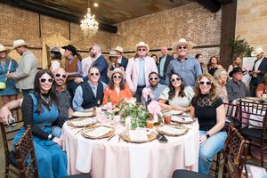 Group of friends wearing sunglasses and cowboy hats gathered around a decorated banquet table at a Western-themed event.