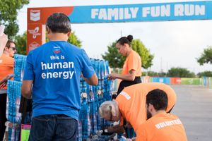 Volunteers in blue and orange shirts set up water stations at a Family Fun Run charity race event outdoors.
