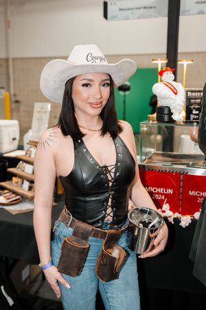 Woman in white cowboy hat and black leather corset top with jeans poses at a Michelin 2024 event.