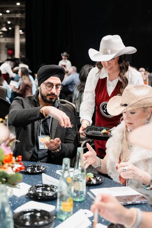 A server in a white cowboy hat presents food to guests at an elegant Western-themed gala dinner event.