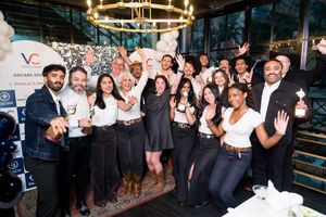 A diverse group of professionals celebrating at a corporate event, posing together with raised hands and drinks.