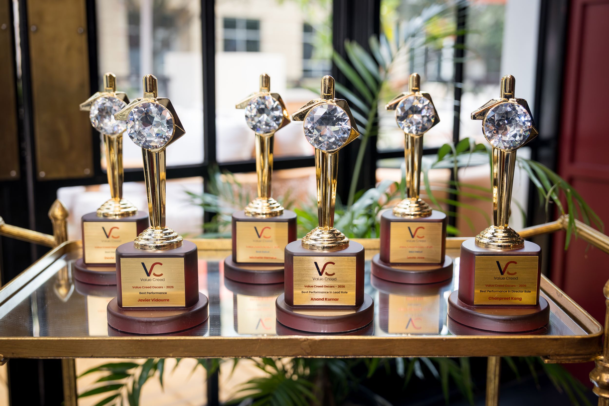 Six gold trophy awards with crystal diamond tops displayed on a mirrored tray, featuring VC logos on wooden bases.
