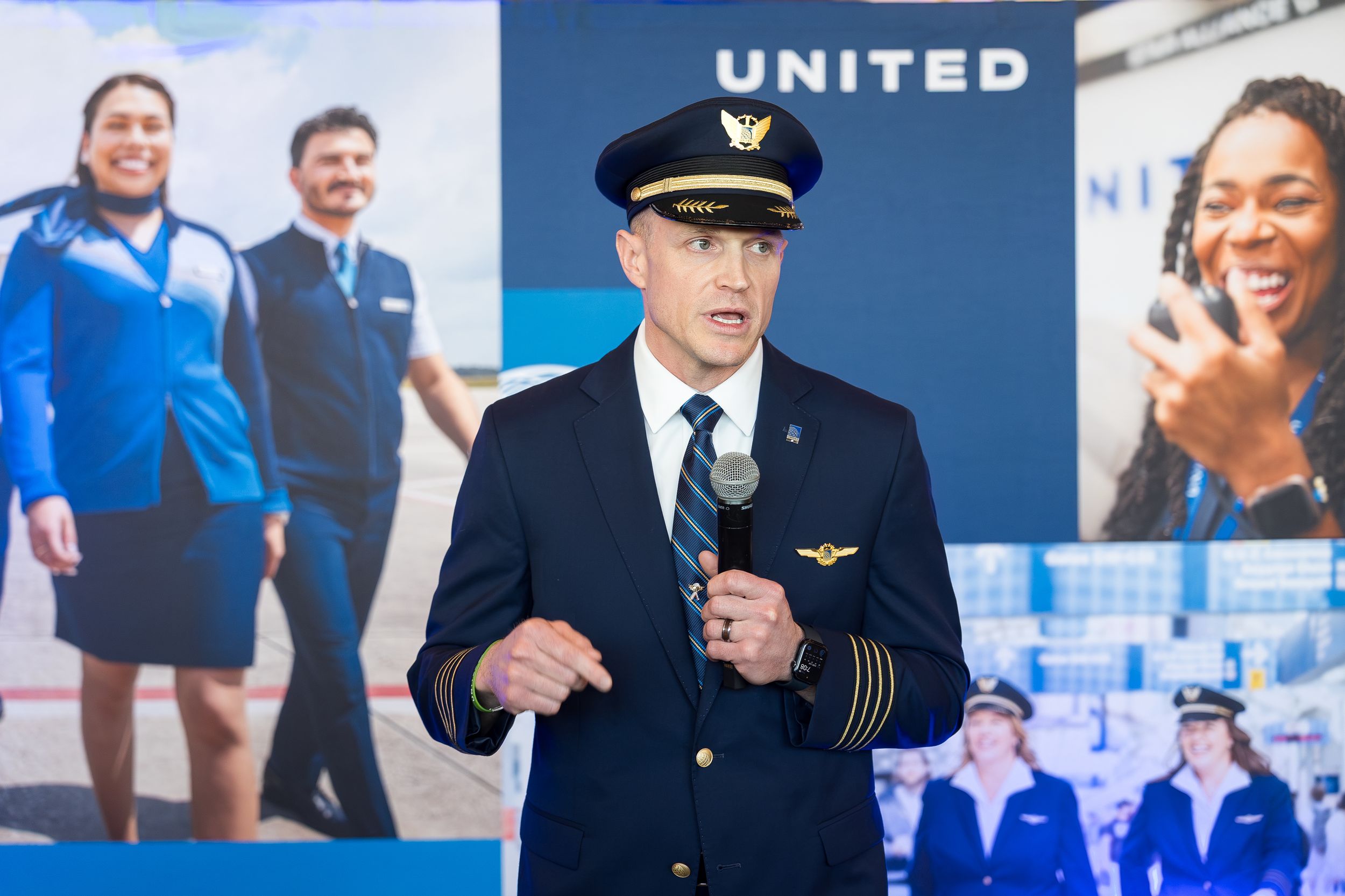 United Airlines pilot in uniform speaks at podium with microphone at corporate event with staff backdrop.