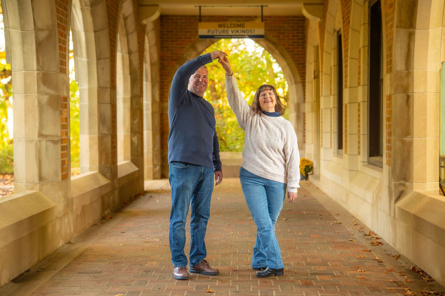A couple walks through a sunlit stone archway corridor with warm golden lighting creating a romantic atmosphere.