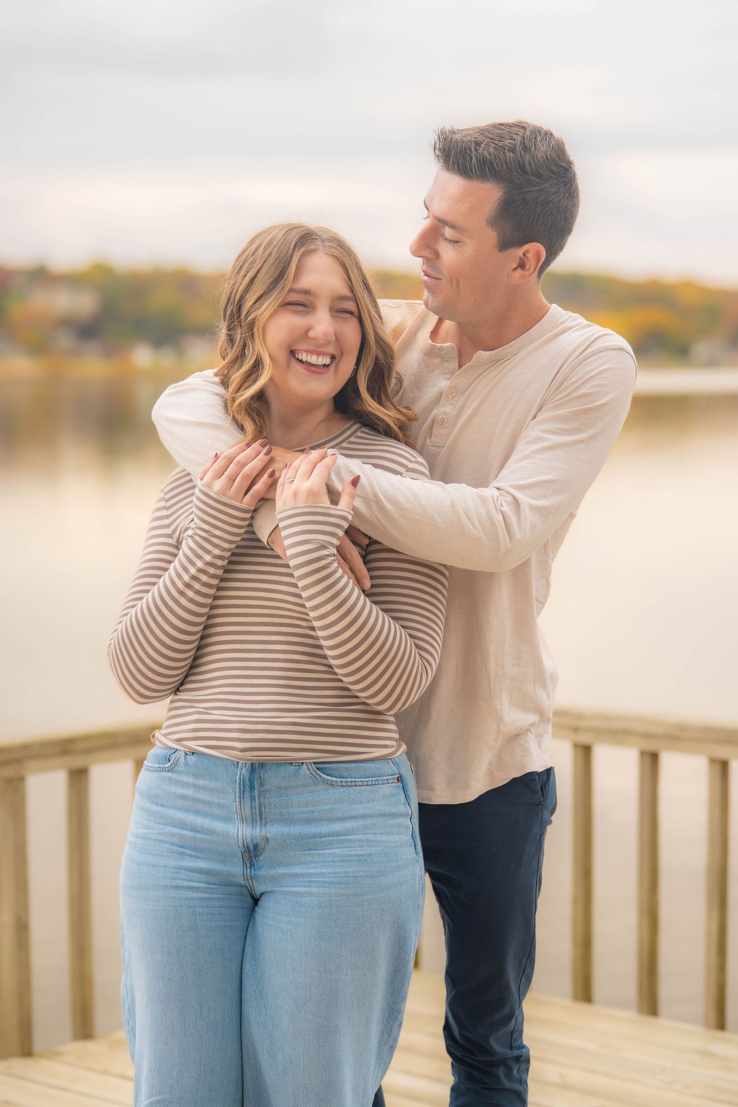 A couple shares a playful moment together on a wooden deck overlooking a lake during golden hour.