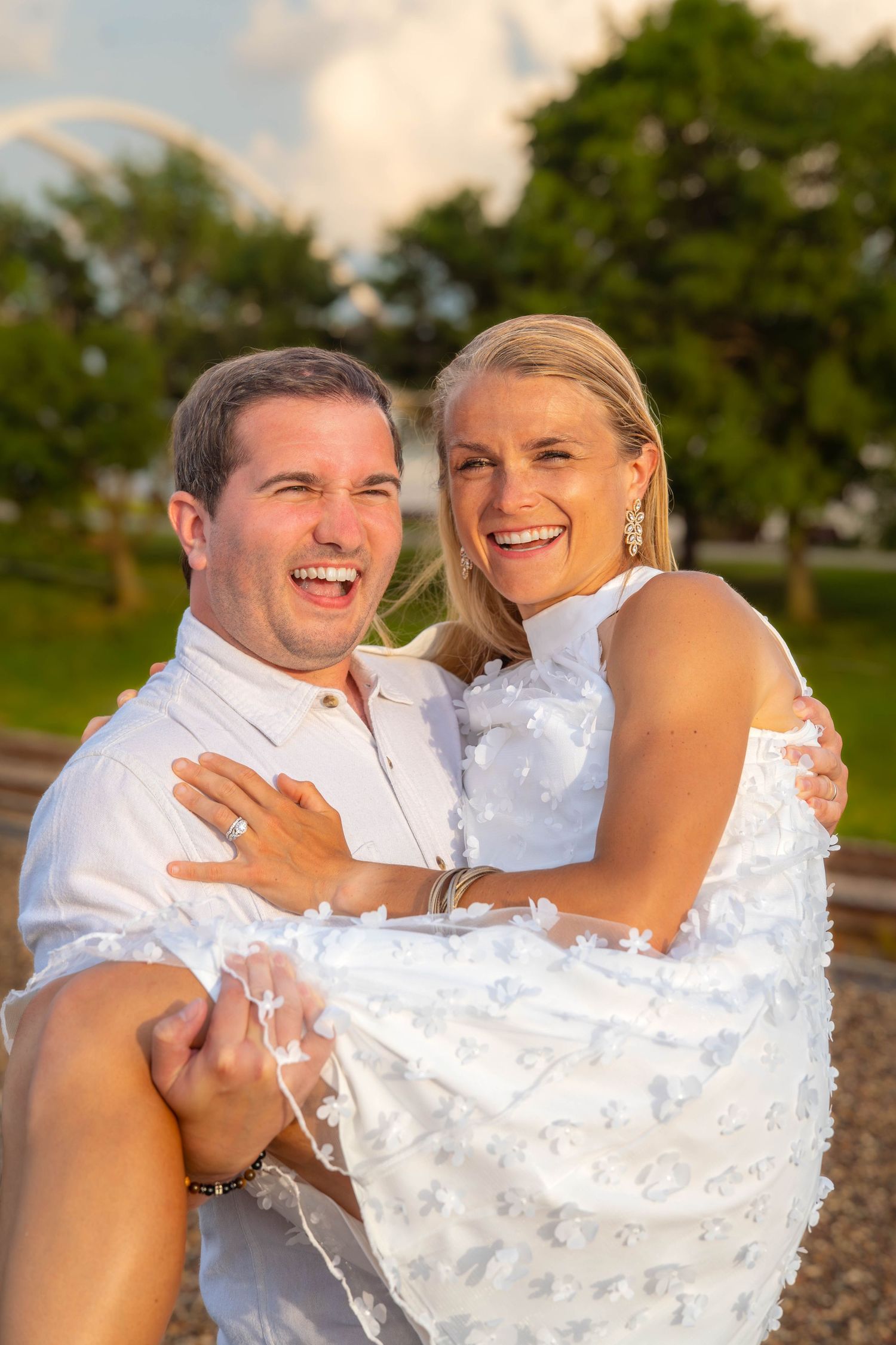 A joyful couple embraces during sunset as the bride's white dress flows in the golden light.