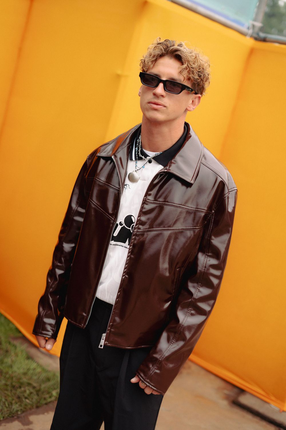 Fashion portrait against vibrant orange wall wearing brown leather jacket and sunglasses.