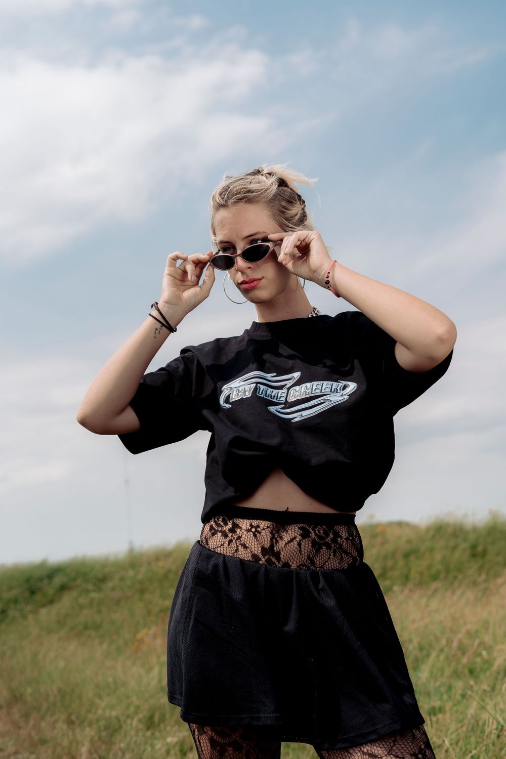 Outdoor fashion sequence in field showing black outfit and sunglasses against cloudy sky.