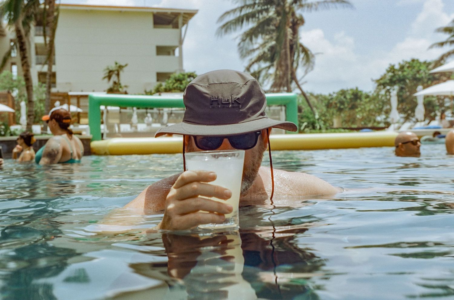 Person enjoying a beverage while swimming in a resort pool on a sunny day.