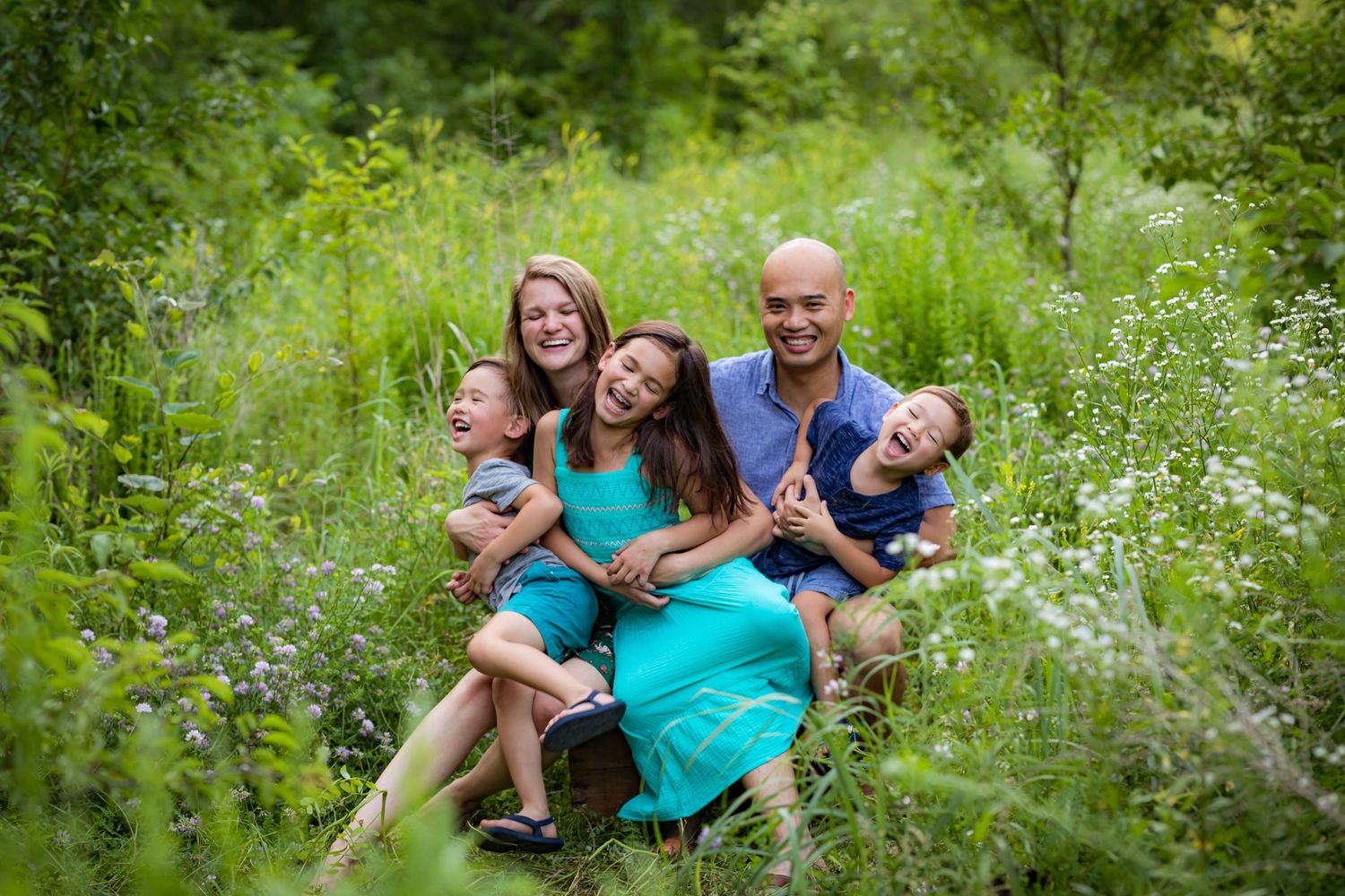 A family enjoying time together while sitting in a lush green meadow with blooming wildflowers on a summer day.