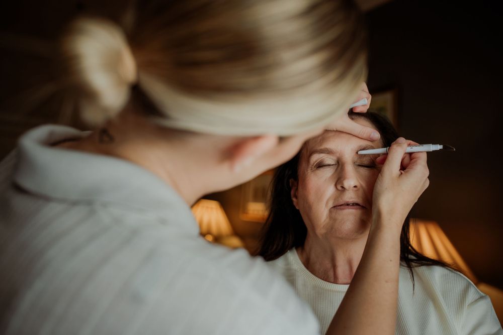 An intimate makeup application moment captured in warm lighting during wedding preparations.