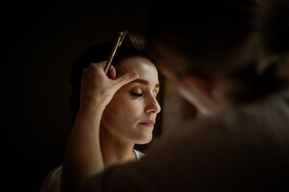 A makeup brush applies eye makeup in dramatic lighting.