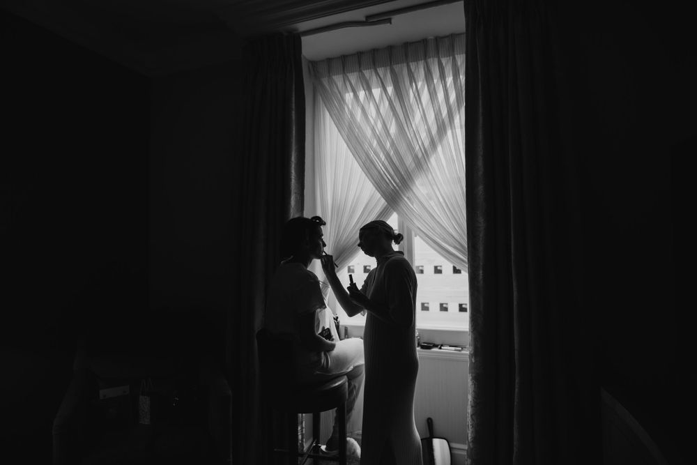 Silhouettes by a window share an intimate moment in black and white photography.  London wedding photographer. The landmark