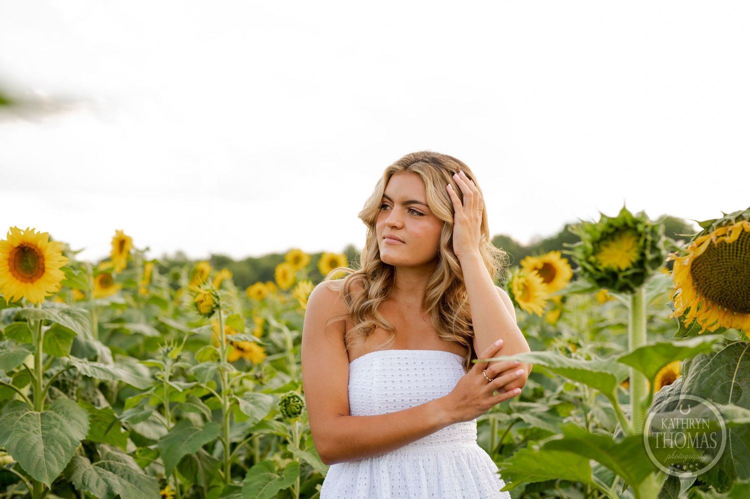 A woman in a white sundress poses gracefully in a vibrant sunflower field.