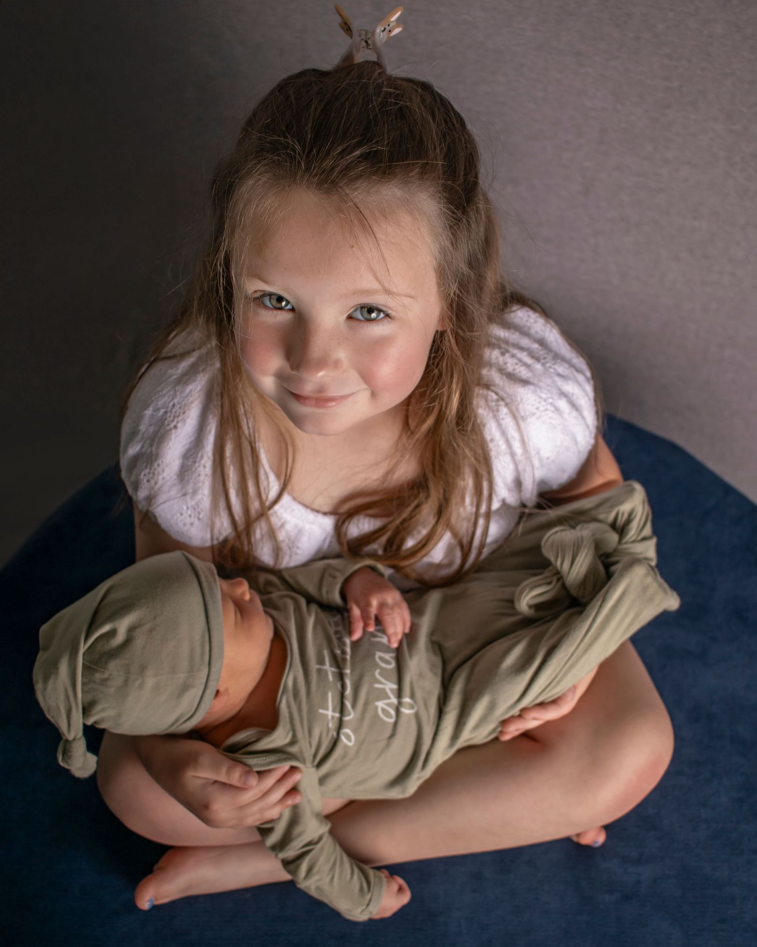 A big sister holds her newborn brother while looking up at the camera.