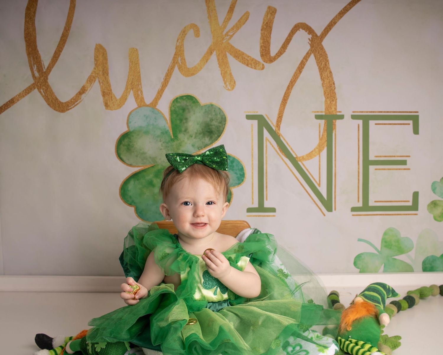 A baby girl sits in front of a "Lucky One" banner with a big smile
