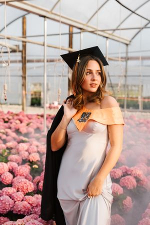 Kayli Basson - 2026 Tahlequah High School senior photo session surrounded by pink hydrangeas and holding her cap and gown.