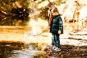 Two brothers play with a stick and stand next to a creek at Coal Creek Farms in Jenks, Oklahoma during their fall family session.