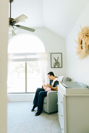 A new dad feeding his newborn daughter during a lifestyle family photography session at their home.