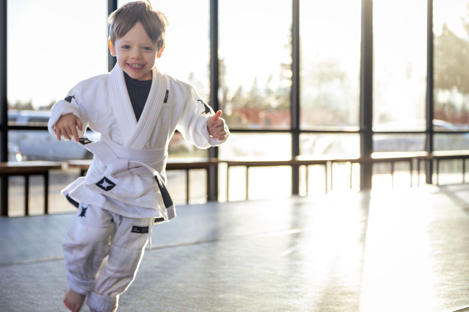 Student practicing martial arts moves in a sunlit dojo with floor-to-ceiling windows.