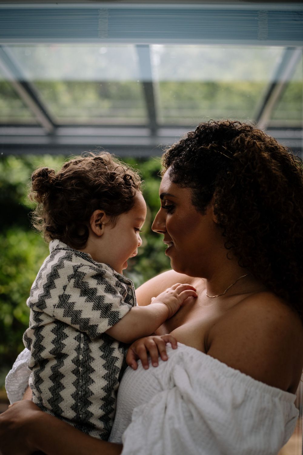 Tender moment between parent and child against a sunlit greenhouse backdrop.