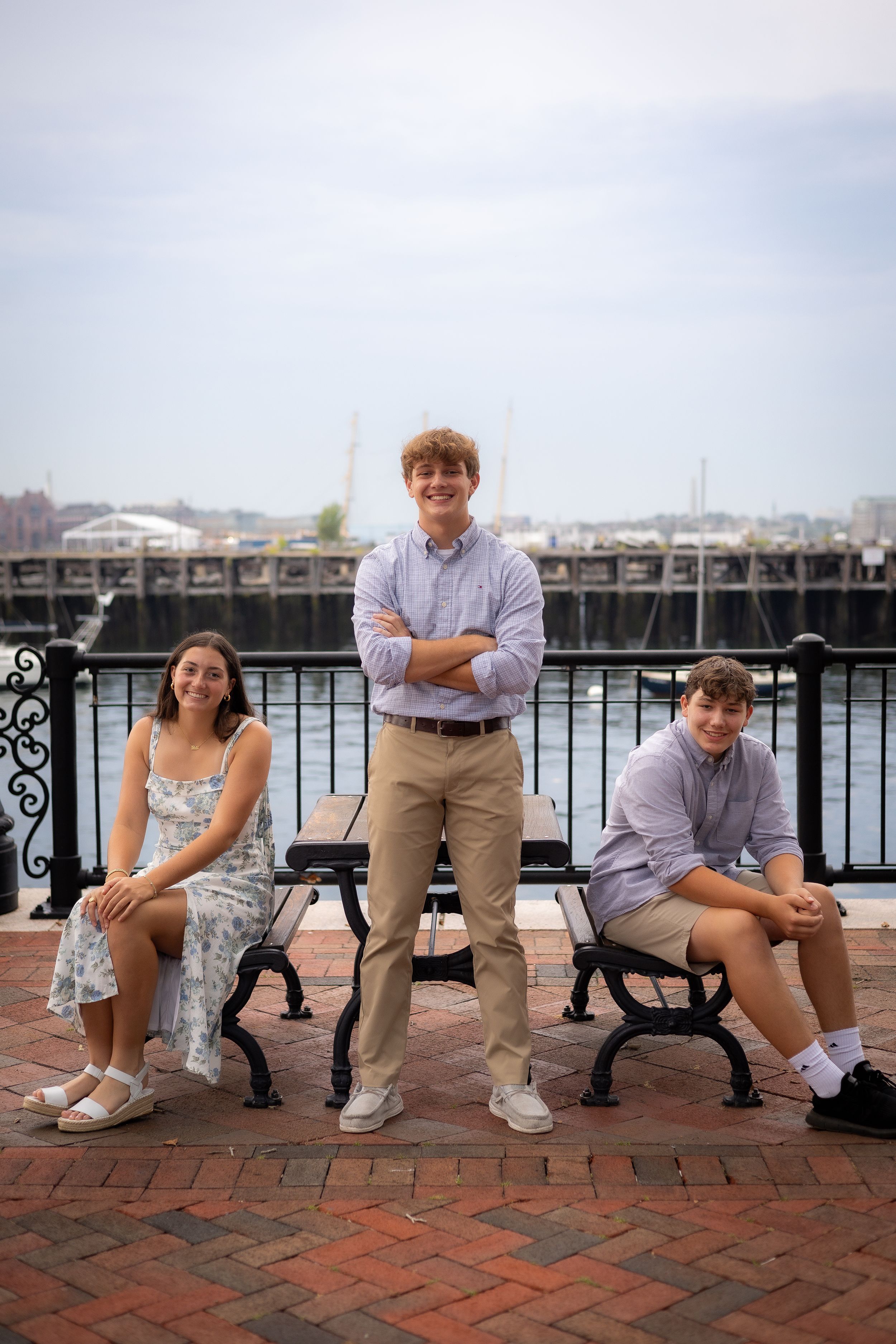 Three people sit on benches along a waterfront boardwalk with a marina in the background.
