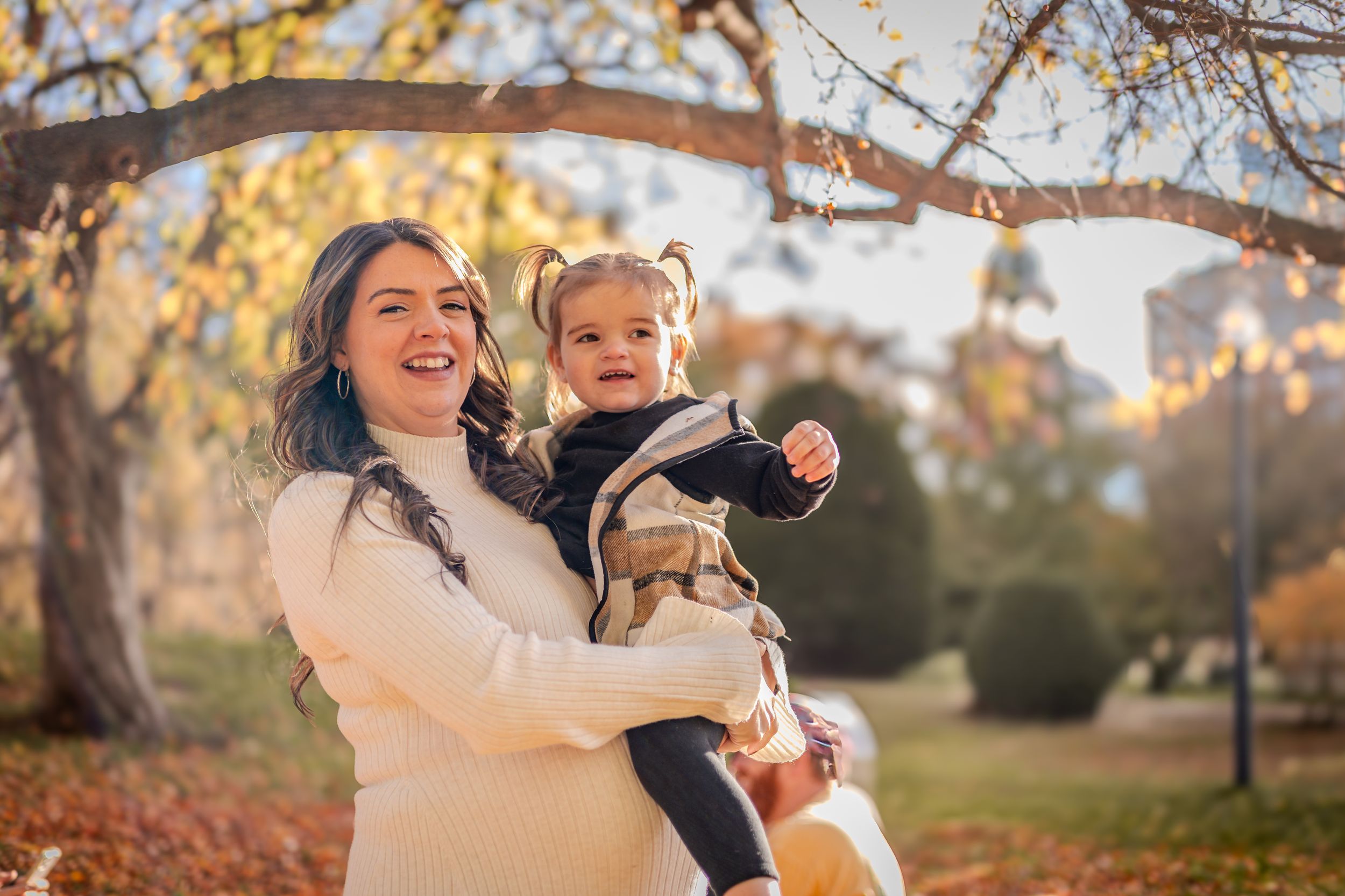 Two people share a joyful moment together while playing in a park during autumn with golden leaves and sunlight.