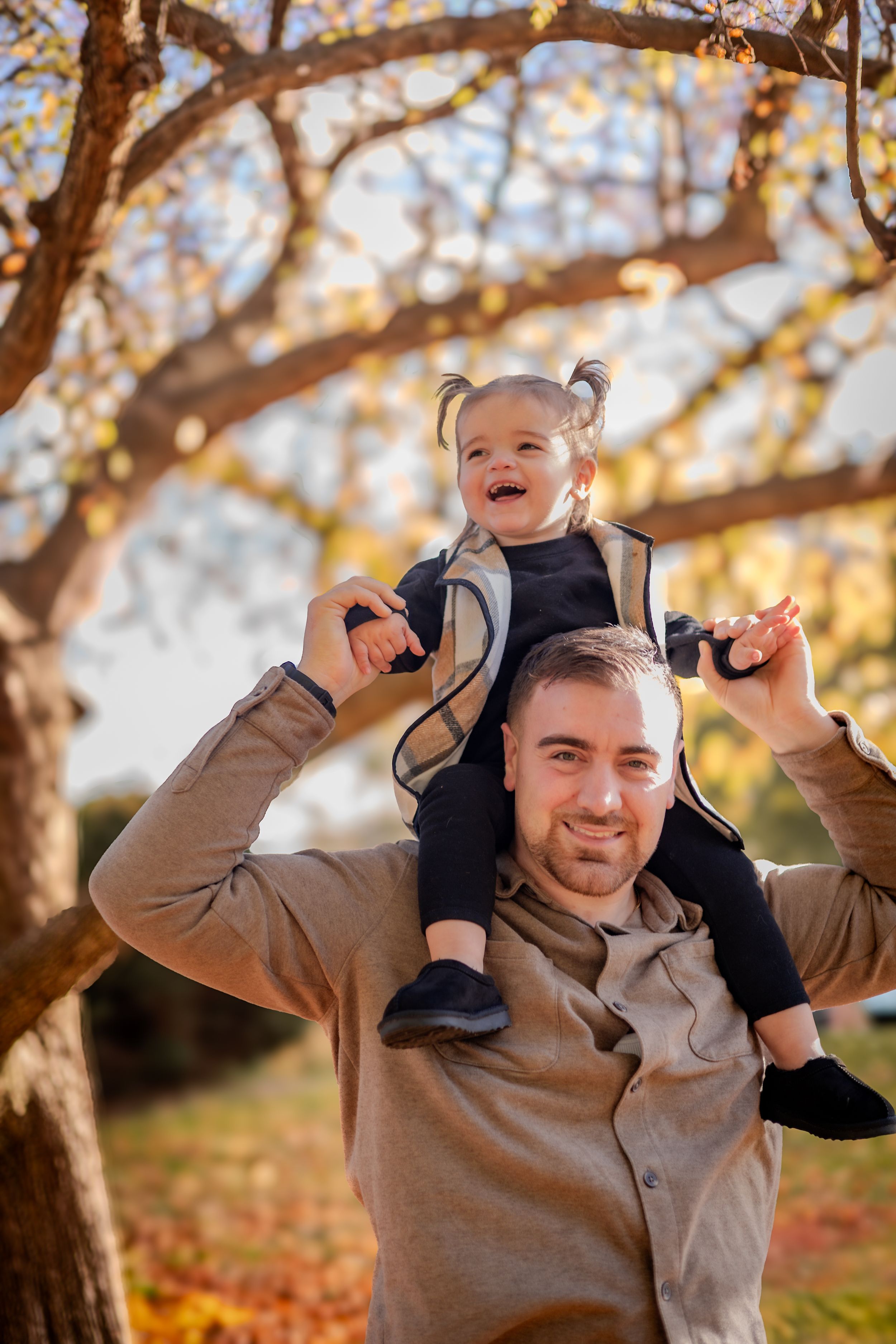 A joyful moment captured outdoors in autumn with a small child riding on shoulders amid golden fall foliage.